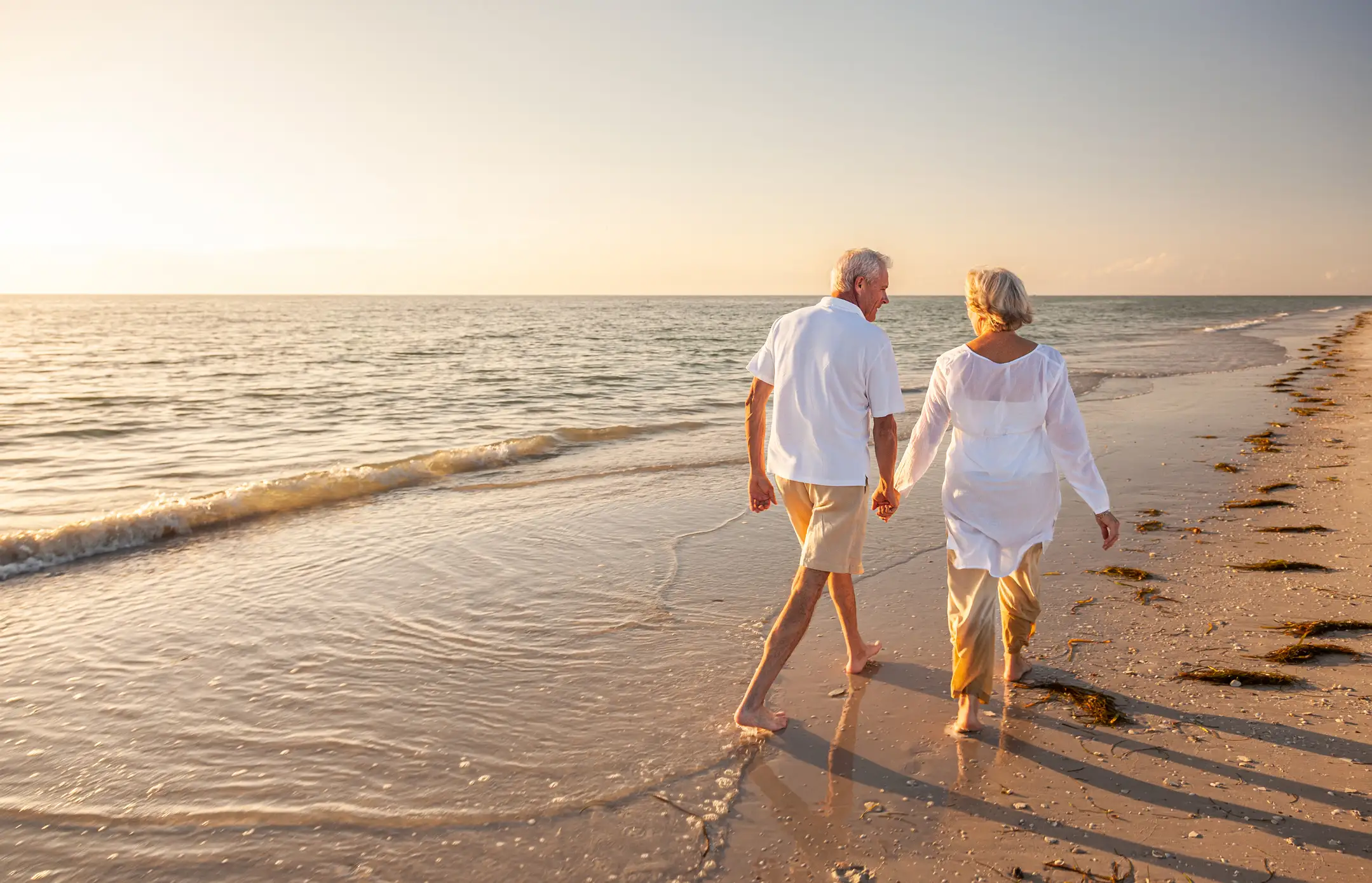 Senior couple walking on a sandy beach at sunrise