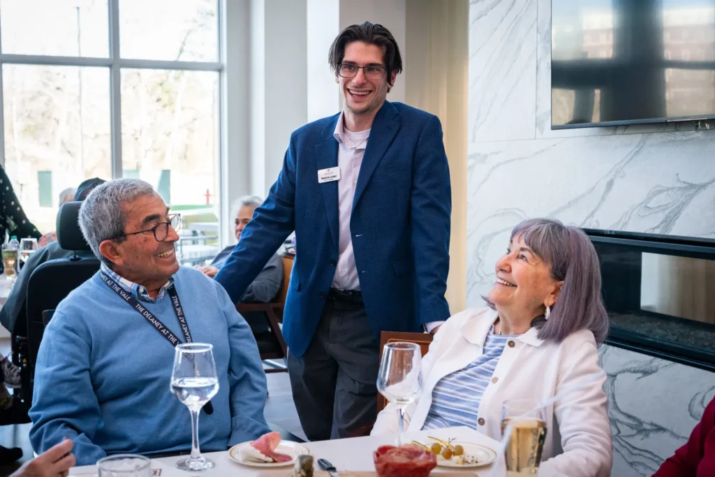 Employee at The Delaney at the Vale checks in with two seniors dining at the community