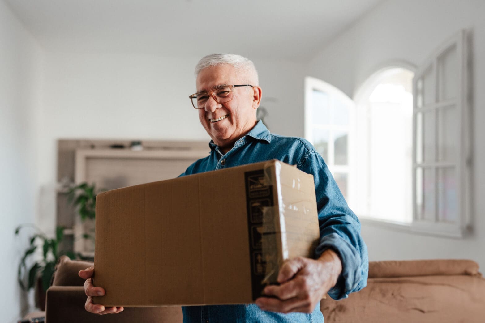 A senior man carrying a box to transition into retirement after learning about 7 senior downsizing tips.