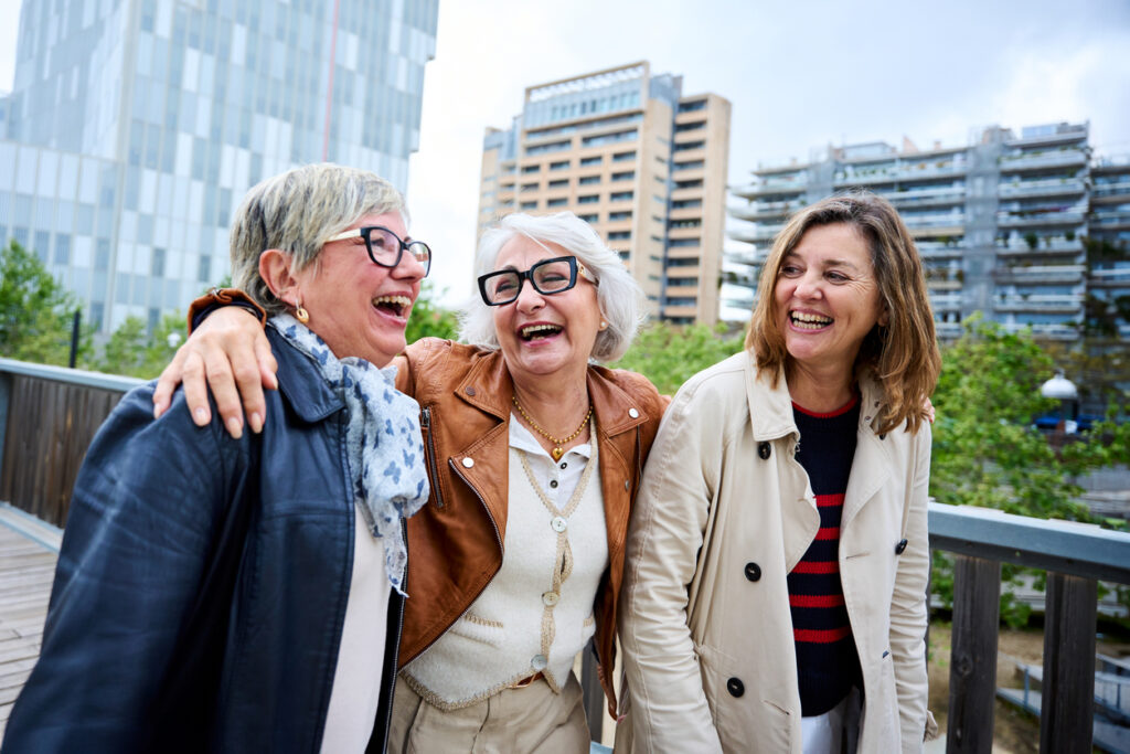 Three cheerful only mature Caucasian friends women enjoying walking happy together in urban park. Older gray hair tourists female people strolling laughing European sightseeing holidays outdoors